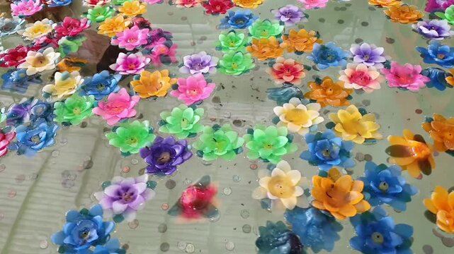Colorful lotus-shaped incense sticks float in pond. At the bottom of pond are coins from prayers, fortune telling, warding off bad luck. Used for worship or decoration. Made from paraffin or beeswax.
