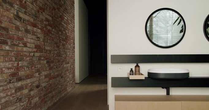 Stylish modern interior showcasing a contrast between a rustic brick wall and sleek minimalist bathroom furnishings with round mirrors and plant reflection. Modern Interior with Brick Wall