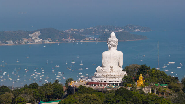 Aerial view of the Big Buddha statue overlooking the turquoise sea and numerous boats in the bay of Tambon Karon, Chang Wat Phuket, Thailand.