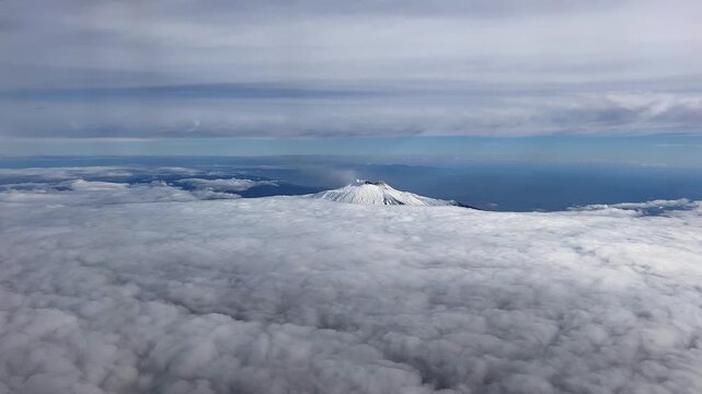 An aerial view of a volcanic crater emitting smoke; Mount Etna rises from a dense layer of clouds in the sky above the Italian island of Sicily 