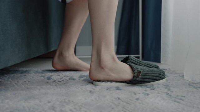 Close-up of a person feet slipping into cozy slippers next to the bed, depicting a calm and relaxing morning routine at home. Relaxing Morning Routine: Putting On Cozy Slippers Beside Bed
