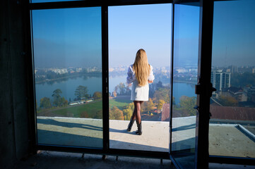 Obraz premium Back view of female property manager standing at balcony entrance of unfinished apartment, showing panoramic view. Concept of residential promotion, property launch, business and advertising use