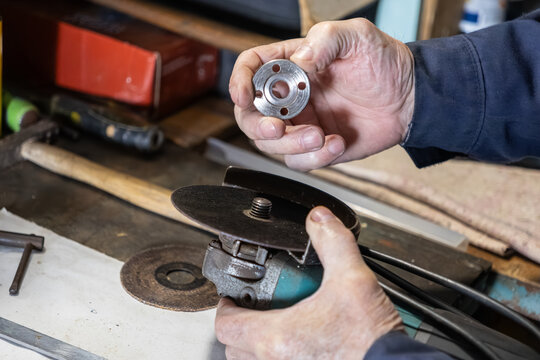 A skilled worker carefully assembles a metal locking nut onto an angle grinder within a workshop, emphasizing industrial precision, professional hardware repair, and tool maintenance