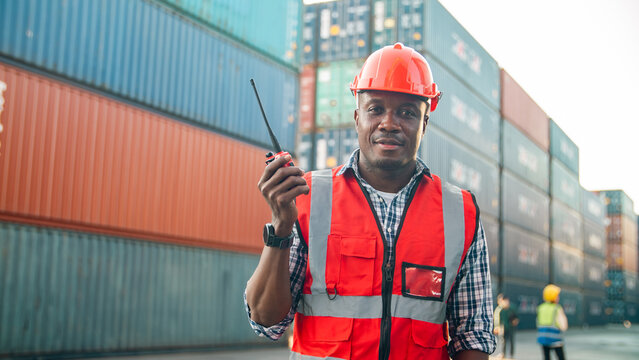 Confident dock worker safety vest hard hat walkie talkie shipping container cargo port logistics supply chain industrial teamwork Confident dock worker wearing safety vest and hard hat holding