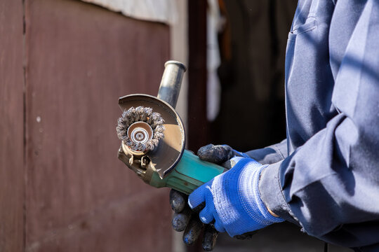 A professional technician holds a portable angle grinder with a wire brush attachment to perform effective metal surface preparation and rust removal tasks within a busy industrial workshop