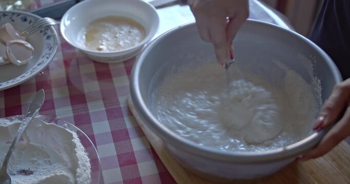 Preparing delicious homemade food. A person vigorously whisks ingredients in a metal bowl, adding liquid. Captures the essence of home cooking and fresh food preparation.