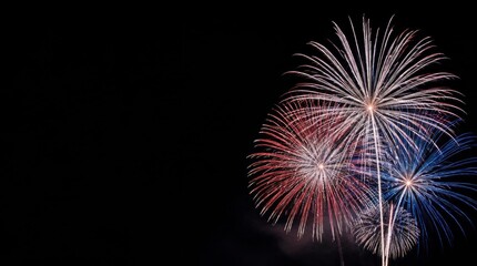 Fototapeta premium Vibrant red white and blue fireworks exploding in night sky with dark background