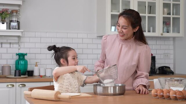 Asian happy mother and little daughter sifting flour with sieve into bowl in kitchen, Family home cooking, baking bakery, childhood learning, motherhood bonding, domestic lifestyle food concept