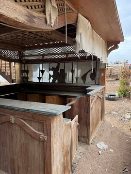 An abandoned wooden stall with a stone countertop. The structure has a rustic design and is partially covered with fabric. Surrounding area appears neglected.