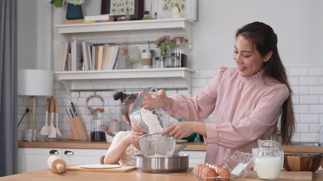 Asian happy mother and little daughter sifting flour with sieve into bowl in kitchen, Family home cooking, baking bakery, childhood learning, motherhood bonding, domestic lifestyle food concept