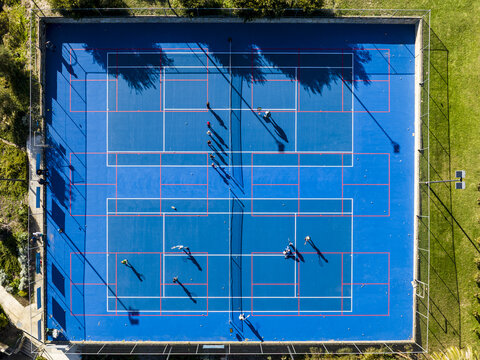 Aerial view of people playing on the blue tennis courts at North Shore Community Hub and Cafe surrounded by green trees in Kallaroo, Western Australia, Australia.