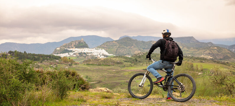 back view of a young male cyclist with mountain bike contemplating the panoramic view of zahara de la sierra, andalusia, spain