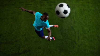 Fototapeta premium Overhead soccer player striking flying ball on green field background. Concept of football action, powerful shot, sports poster design, match promotion and athletic gear campaign.