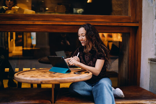 She scrolls or taps on tablet screen with stylus in motion, smiling softly &mdash; a moment of digital browsing or design work, showing ease and fluency with tech in modern freelance life.