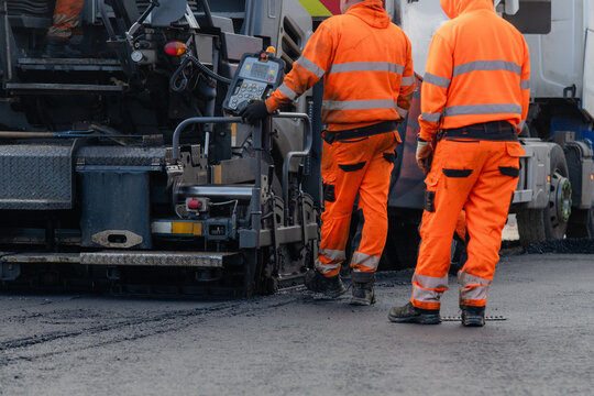 Road workers lay asphalt on a busy street in the morning while operating heavy equipment and wearing safety clothing