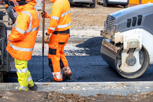 Workers lay asphalt on a construction site while using machinery and equipment in broad daylight