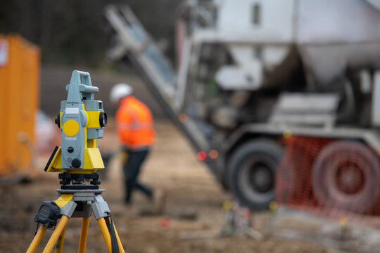 Survey equipment stands in focus with construction truck and worker in the background at a work site during daytime