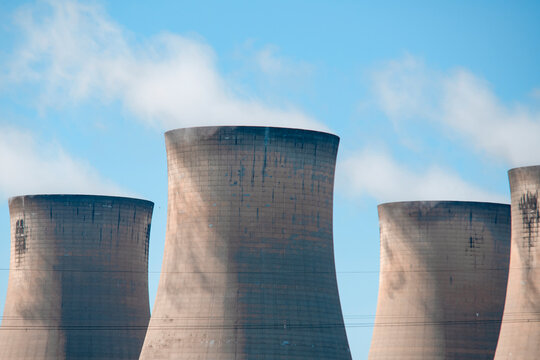 Cooling towers stand tall against a clear blue sky in an industrial area during a sunny day in the afternoon
