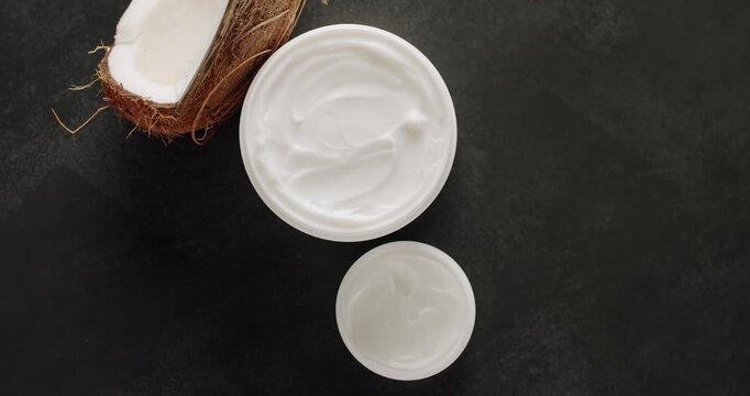 Cosmetics oils based on natural ingredients, scrub, tonic, body care. Cosmetic bottles, Jars and tubes with coconut for cosmetics and Beauty treatment spin on a black background. Top view.