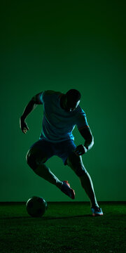 Soccer player dribbling ball in dark green studio sport scene. Concept of football agility, speed training, athletic gear campaign, coaching content and match preparation.