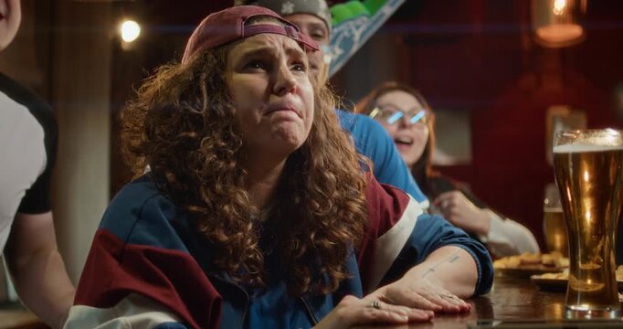 Low angle shot of young woman taking her cap off in dispair as her football team losing intense match, watching game at bar