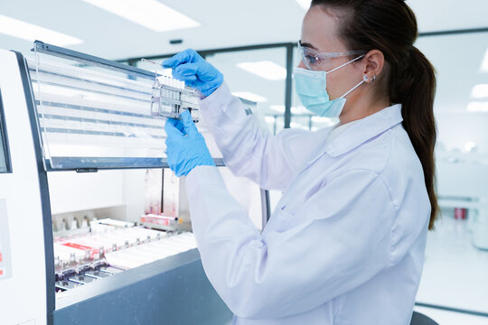 Medical scientist loading slide rack into automated stainer machine. Lab technician in protective gear processing histology samples in sterile hospital laboratory.