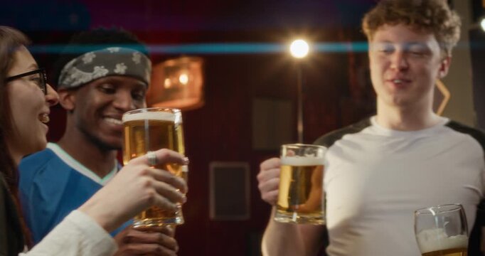 Low angle shot of four friends, smiling warmly, clinking their tall glasses of beer and chatting at the bar