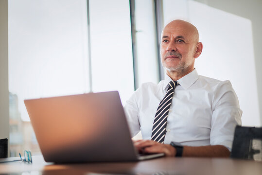 Confdient businessman wearing business casual and and using laptop in a modern bright office