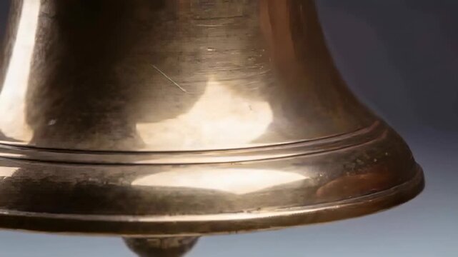 Touching right thumb on rim, right hand rotating brass bell in studio, inspecting internal clapper