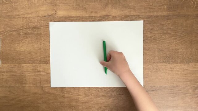 child hands placing green pen on white paper on wooden table slow motion 4K