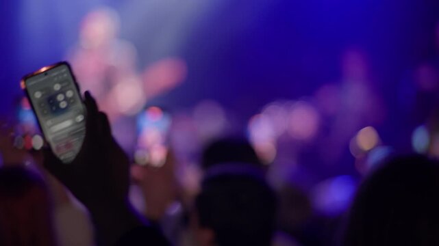 Several audience members raise smartphones to film performance, purple and teal stage light, performer on stage blurred in upper background