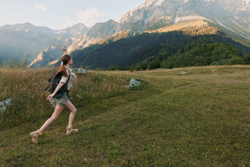Naklejka premium Young woman hiking in a grassy mountain meadow, exploring nature under blue skies, carrying a light backpack, and enjoying fresh air. Her casual outdoor outfit and sturdy boots convey a relaxed,