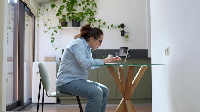 Woman remote working with rounded back, poor posture while using laptop at home. Unhealthy sitting habits, back pain and strain from prolonged computer use. Physical discomfort, risk of spinal issues