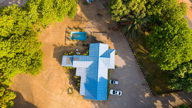 Aerial view of a building with a bright blue roof, a swimming pool, and surrounding green trees in Kaduna, Kaduna, Nigeria.
