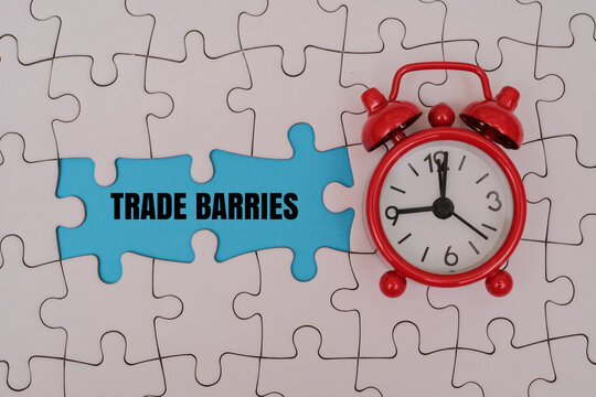 TRADE BARRIES word alphabet letters on puzzle next to red alarm clock. Global commerce, tariffs, quotas and economic concept