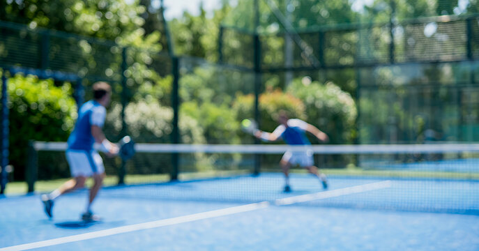 Motion blurred tennis players compete on an outdoor court surrounded by greenery, producing a dreamy and vibrant scene suitable for fitness, recreation, and active lifestyle concepts.