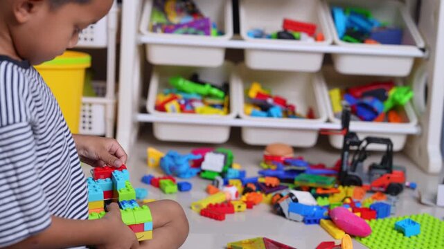 Child playing with colorful plastic building blocks on the floor, hands assembling toy bricks, early learning, creativity, motor skills development, education concept, playful childhood activity.