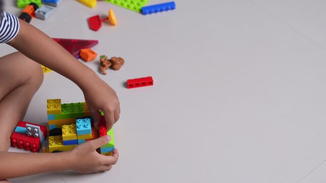 Child playing with colorful plastic building blocks on the floor, hands assembling toy bricks, early learning, creativity, motor skills development, education concept, playful childhood activity.