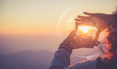 Naklejka premium Hands framing the sun with futuristic digital hologram overlay at sunset. Future vision and technology concept.
