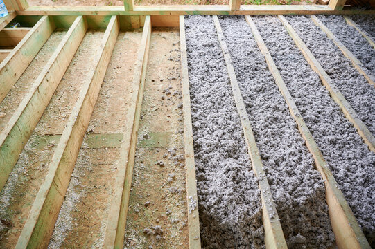 Paper insulation fills floor cavities of timber frame house during construction. Unfinished wooden structure interior, thermal protection, eco building material and energy efficiency concept.