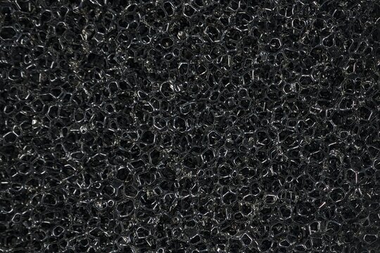 Abstract macro shot of black porous sponge cellular foam texture.