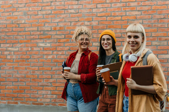 Diverse student friends walking on campus drinking coffee