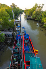 Fototapeta premium Two Traditional Thai Longtail Fishing Boats Moored in a Mangrove Canal at Sunset,High-angle view of two vibrant red and green traditional longtail fishing boats docked side-by-side in a narrow canal.