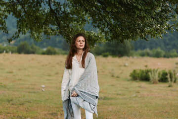 Naklejka premium Woman in a gray shawl stands in an open field, natural lifestyle portrait, calm mood, soft light, outdoor countryside setting, serene and relaxed, she gazes into distance, casual pose, windswept
