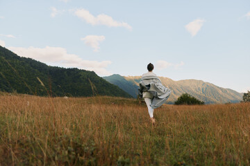 Naklejka premium Woman walking through a tall grass field toward distant mountains, embracing outdoor living, calm sunlight, free spirit, natural landscape, serene mood, in the golden hour breeze quiet sky above.