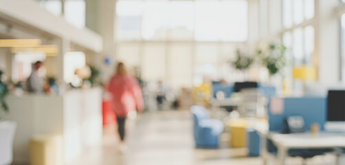 A blurred office environment featuring bright, natural light, modern furniture, and people engaged in various activities, creating a lively work atmosphere. © Wisnu