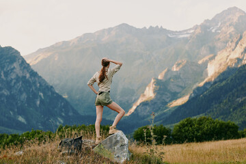 Naklejka premium A woman stands on a rock in an alpine meadow, looking toward distant peaks, capturing a moment of outdoor adventure, personal exploration, and calm freedom.
