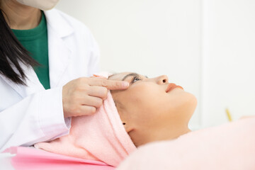 Fototapeta premium Woman relaxes with closed eyes during a facial treatment. Practitioner gently adjusts her face with precise fingers. Her smile reflects calm and pleasure from the care 