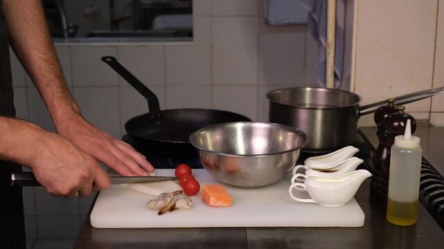 Chef cutting seafood for marinade on cutting board in professional restaurant kitchen close-up of hands

