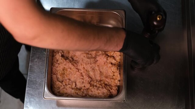 Chef in black rubber gloves salting and peppering freshly made minced meat top view close-up of hands

